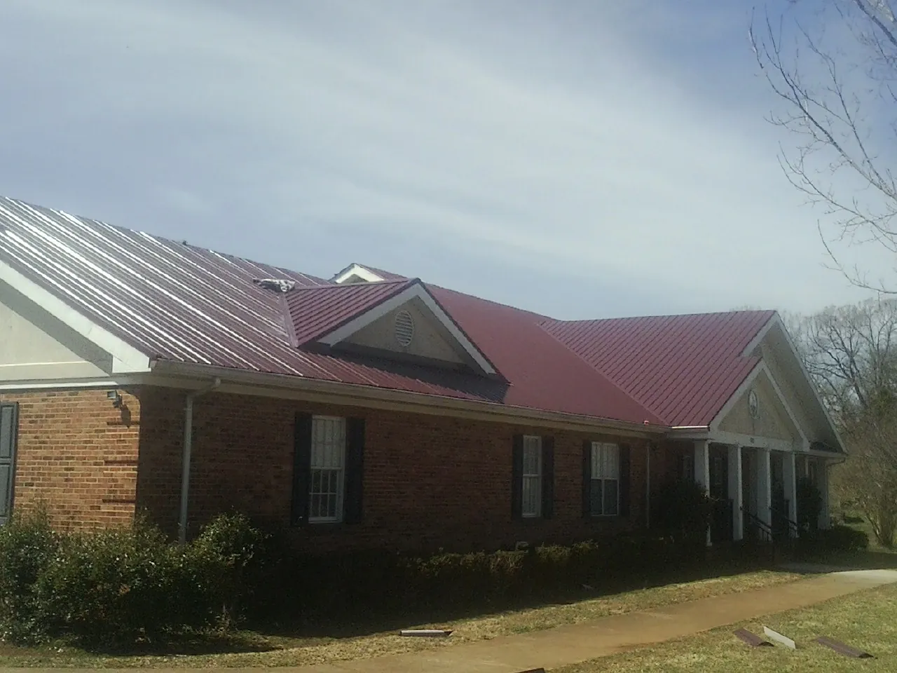 Red metal roof with gabled entries on a long brick building, from a Hail Damage Roof Repair job in Chelan