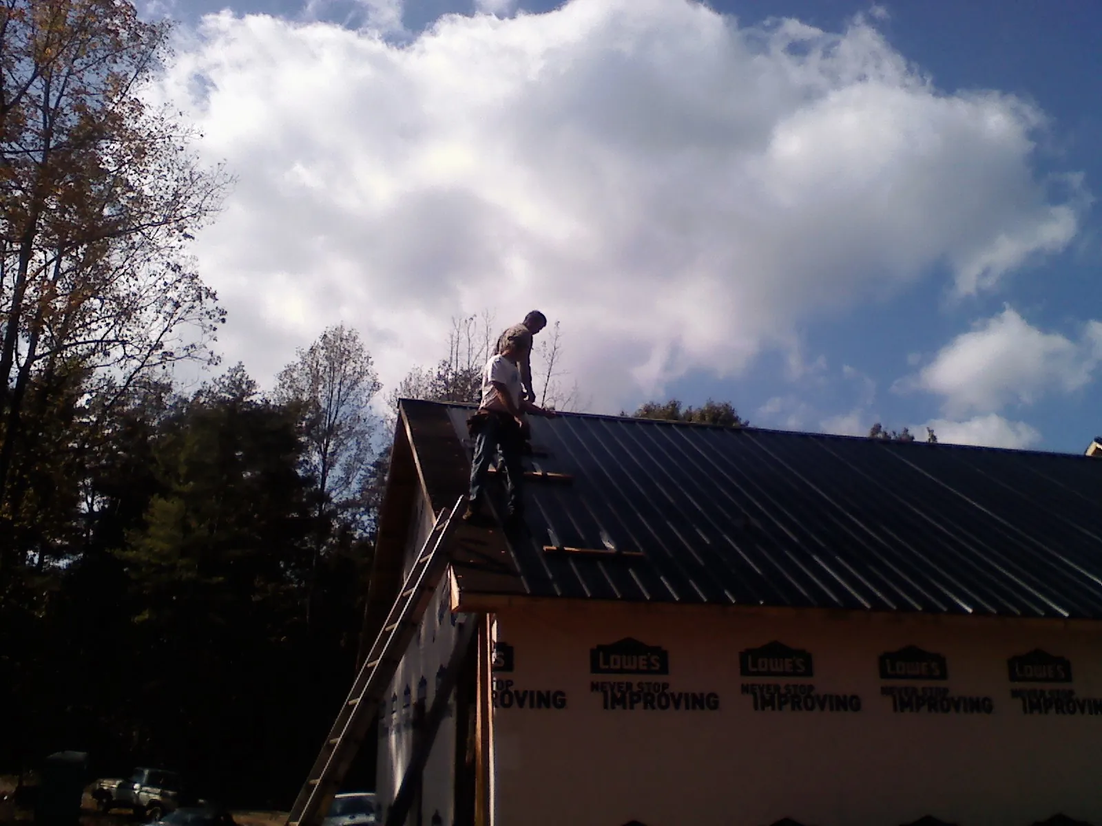 Roofer fastening dark metal panels high against a cloudy sky, from a Roof Inspection job in Chelan